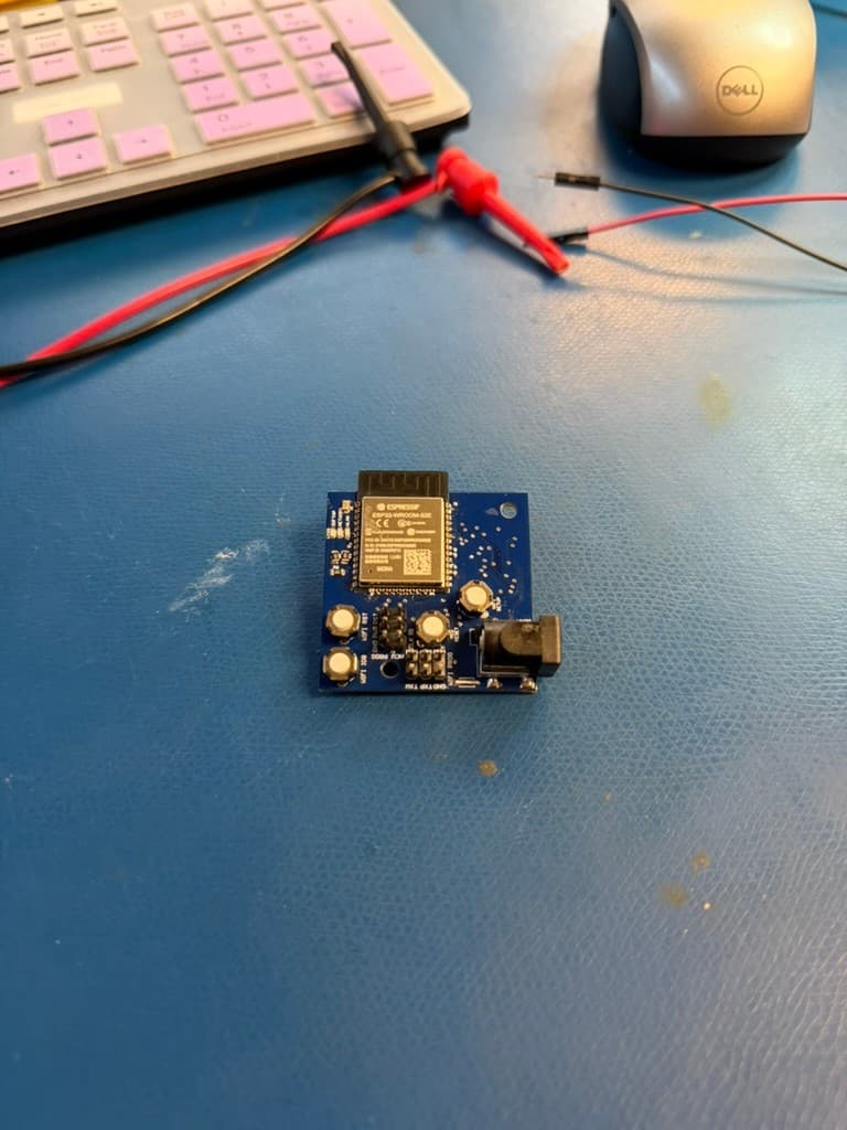 Compact blue custom webcam PCB populated with an ESP32 module, buttons, connectors, and power input